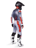 Pilote de motocross de profil arrière portant un maillot Supertech Lipan 2025 et un pantalon assorti en gris et orange fluo, avec le marquage Alpinestars orange vif sur les manches et les jambes, associé à un casque noir et des bottes blanches, tenue professionnelle coordonnée pour la course tout-terrain