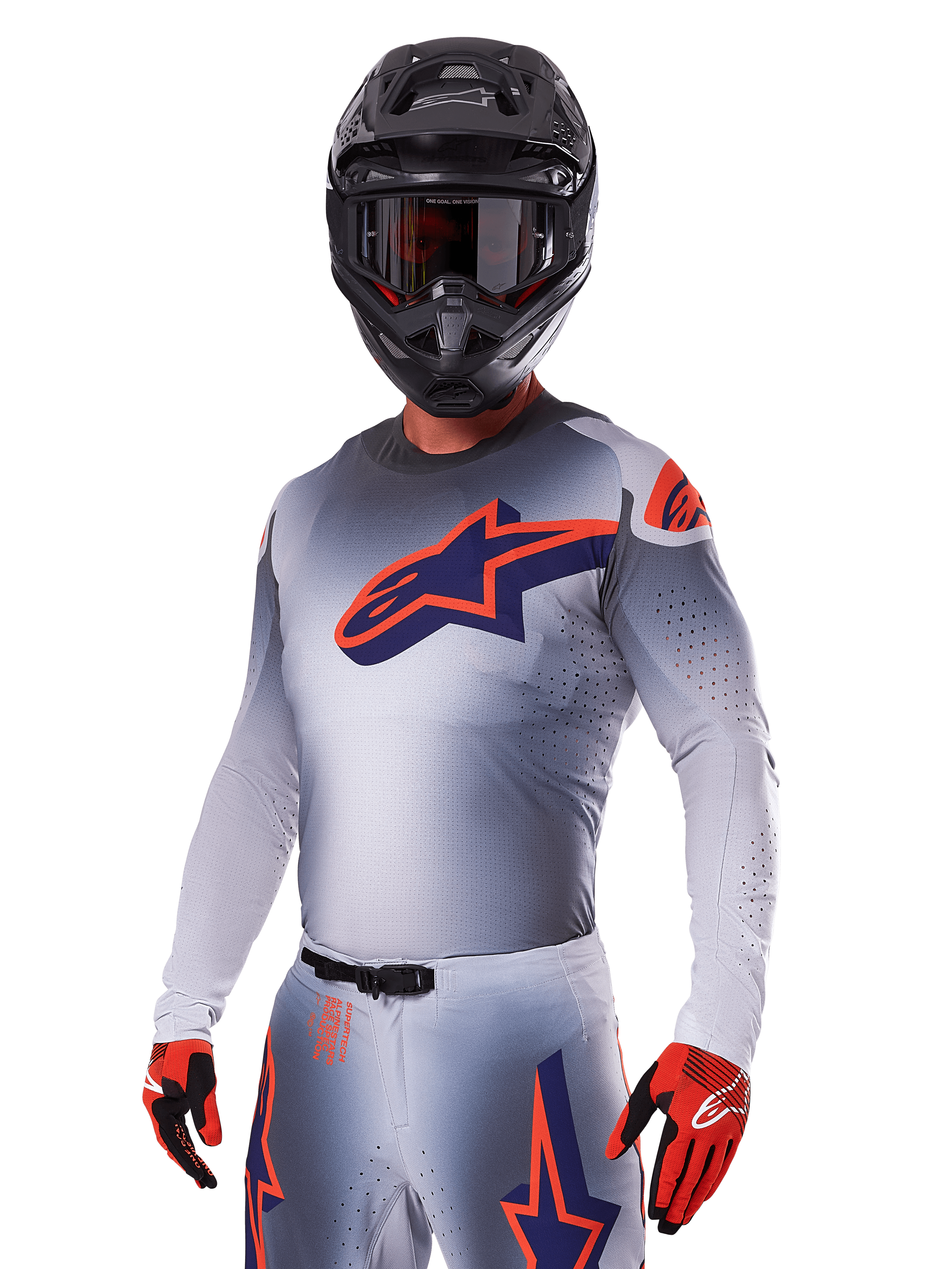 Pilote de motocross portant l'ensemble Alpinestars Supertech Lipan 2025, maillot et pantalon gris avec accents bleu marine et orange, casque noir mat avec lunettes, gants rouges et noirs, équipement de performance athlétique pour la course tout-terrain