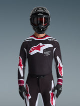 Alpinestars 2026 Supertech AFD Vista Jersey, maillot de motocross noir, rouge et blanc, présenté sur un pilote avec un casque noir, des lunettes et des gants, arborant un large logo sur la poitrine et le marquage « SUPERTECH AFD », équipement de course professionnel pour la performance tout-terrain