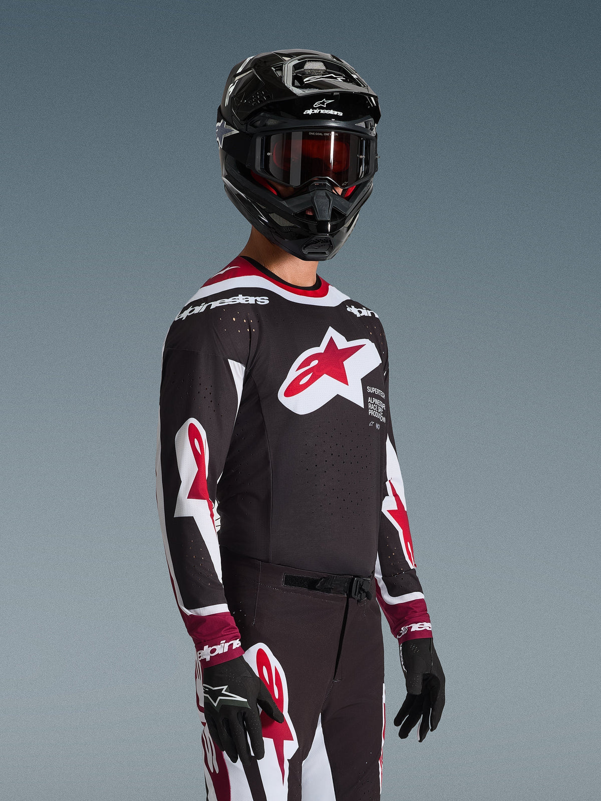 Motocross rider wearing the Alpinestars 2026 Supertech AFD Vista Jersey in Black Red and White, featuring a large red star logo on the chest and laser-cut perforations, paired with a black helmet and matching racing pants for off-road performance