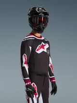 Pilote de motocross portant le maillot Alpinestars Supertech AFD Vista 2026 noir, rouge et blanc, arborant un grand logo étoile rouge sur la poitrine et des perforations découpées au laser, associé à un casque noir et un pantalon de course assorti pour la performance tout-terrain