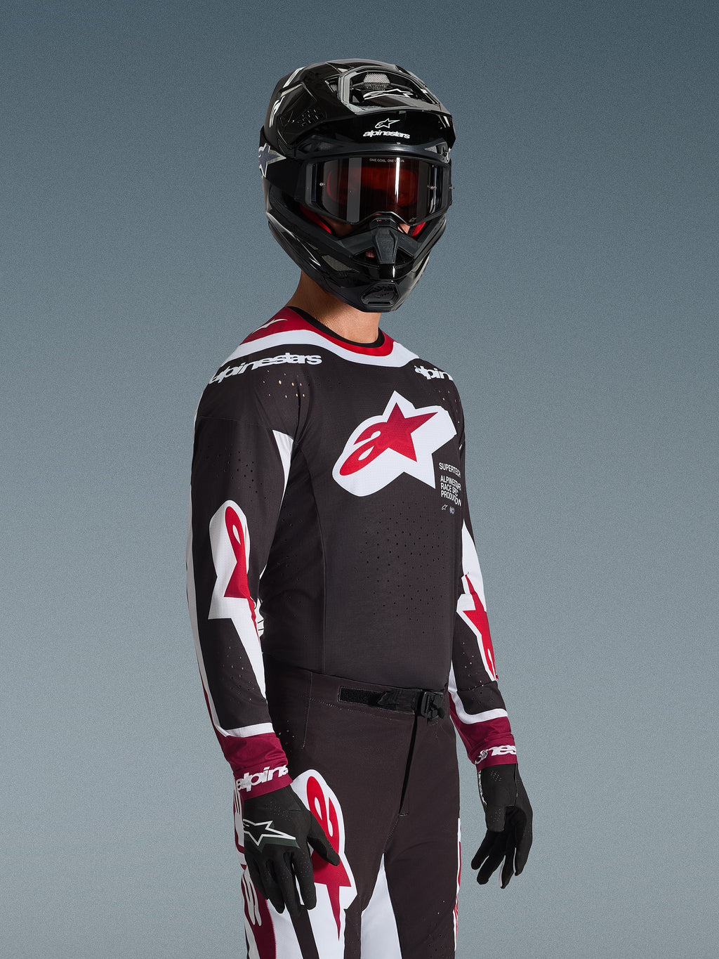 Maillot Alpinestars 2026 Supertech AFD Vista, pilote de motocross portant un équipement de course complet, maillot noir avec des accents rouges et blancs, grand logo sur la poitrine, perforations découpées au laser, porté avec un pantalon assorti, un casque noir et des lunettes rouges, tenue coordonnée pour la course tout-terrain