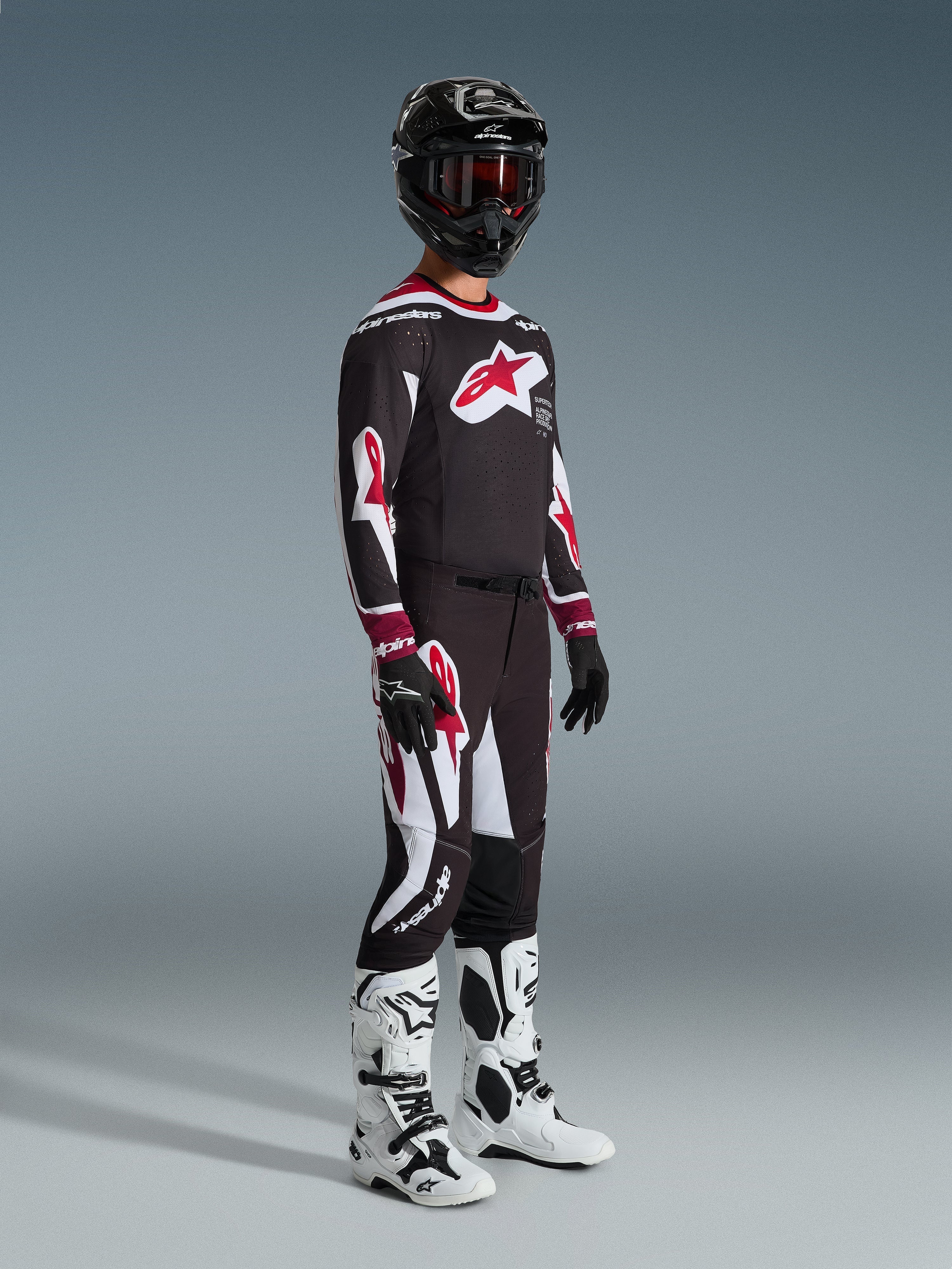 Motocross rider wearing complete racing gear, 2026 Supertech AFD Vista Jersey in Black Red and White, matching motocross pants, black helmet with red goggles, white and black boots, black and white gloves, coordinated outfit for professional off-road racing