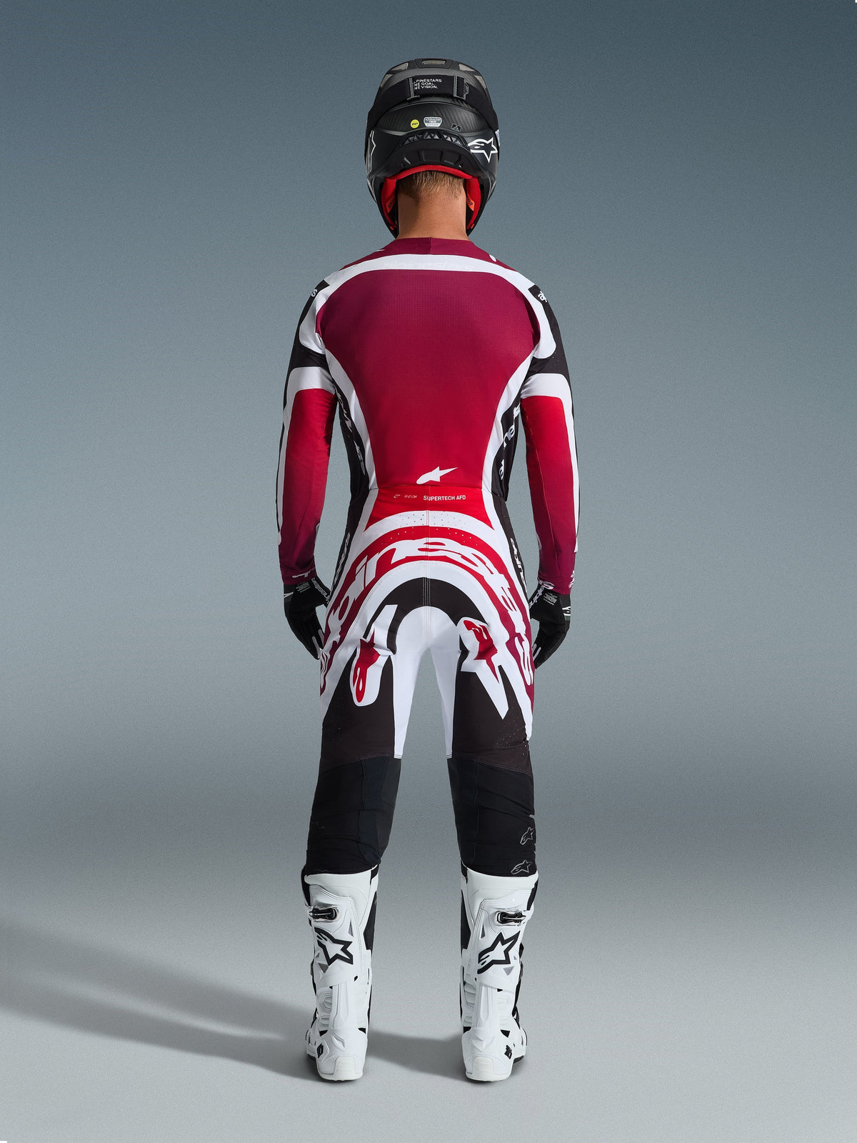 Motocross rider from behind wearing the 2026 Supertech AFD Vista Jersey in Black, Red, and White, paired with matching motocross pants, black helmet, and white boots, complete professional racing gear set for off-road competition