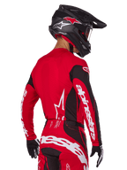 Motocross rider from back view wearing Alpinestars 2025 Techstar Dreem Gear Set, Red and black jersey with white sleeve branding, matching red and black pants with bold white logo on the seat, black carbon helmet with red accents, black and white gloves, professional off-road racing outfit.