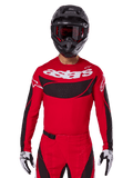Alpinestars 2025 Techstar Dreem Jersey, équipement de motocross, rouge vif et noir, avec logo 'astars' blanc et empiècement de poitrine ventilé noir, porté avec pantalon assorti, casque noir et gants blancs et noirs, conçu pour la course tout-terrain professionnelle