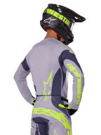 Pilote de motocross de dos portant l'ensemble Alpinestars Techstar Dreem 2025, maillot et pantalon gris avec marquages jaune-vert fluo, casque noir assorti avec graphismes fluo, tenue de course professionnelle