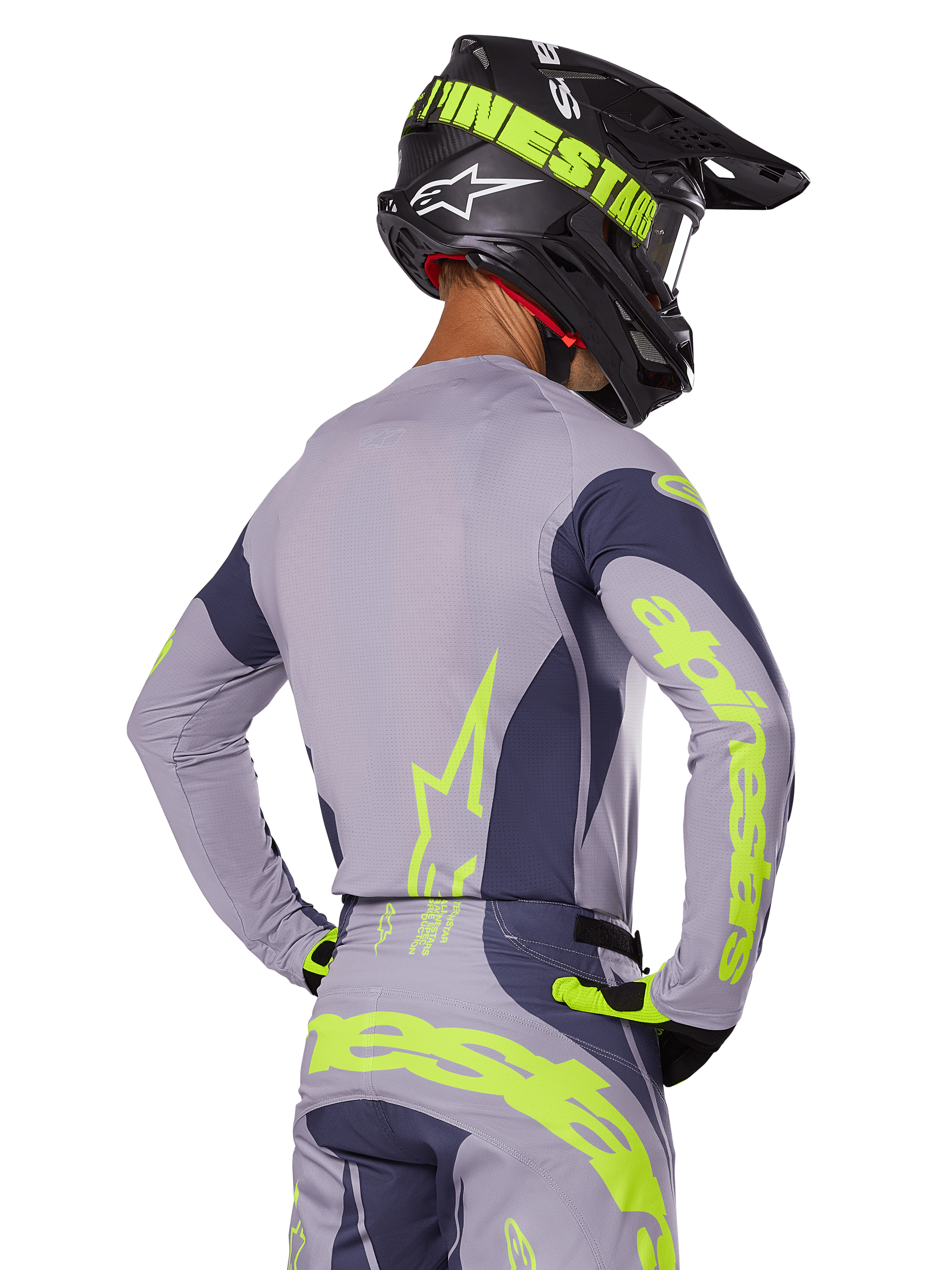 Pilote de motocross de dos portant l'ensemble Alpinestars Techstar Dreem 2025, maillot et pantalon gris avec marquages jaune-vert fluo, casque noir assorti avec graphismes fluo, tenue de course professionnelle