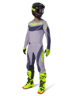 Pilote de motocross portant le maillot Techstar Dreem 2025 en gris et gris foncé avec des accents jaune fluo, tenue de course complète incluant un pantalon gris assorti, des bottes et des gants jaune fluo et un casque noir, équipement de performance tout-terrain coordonné