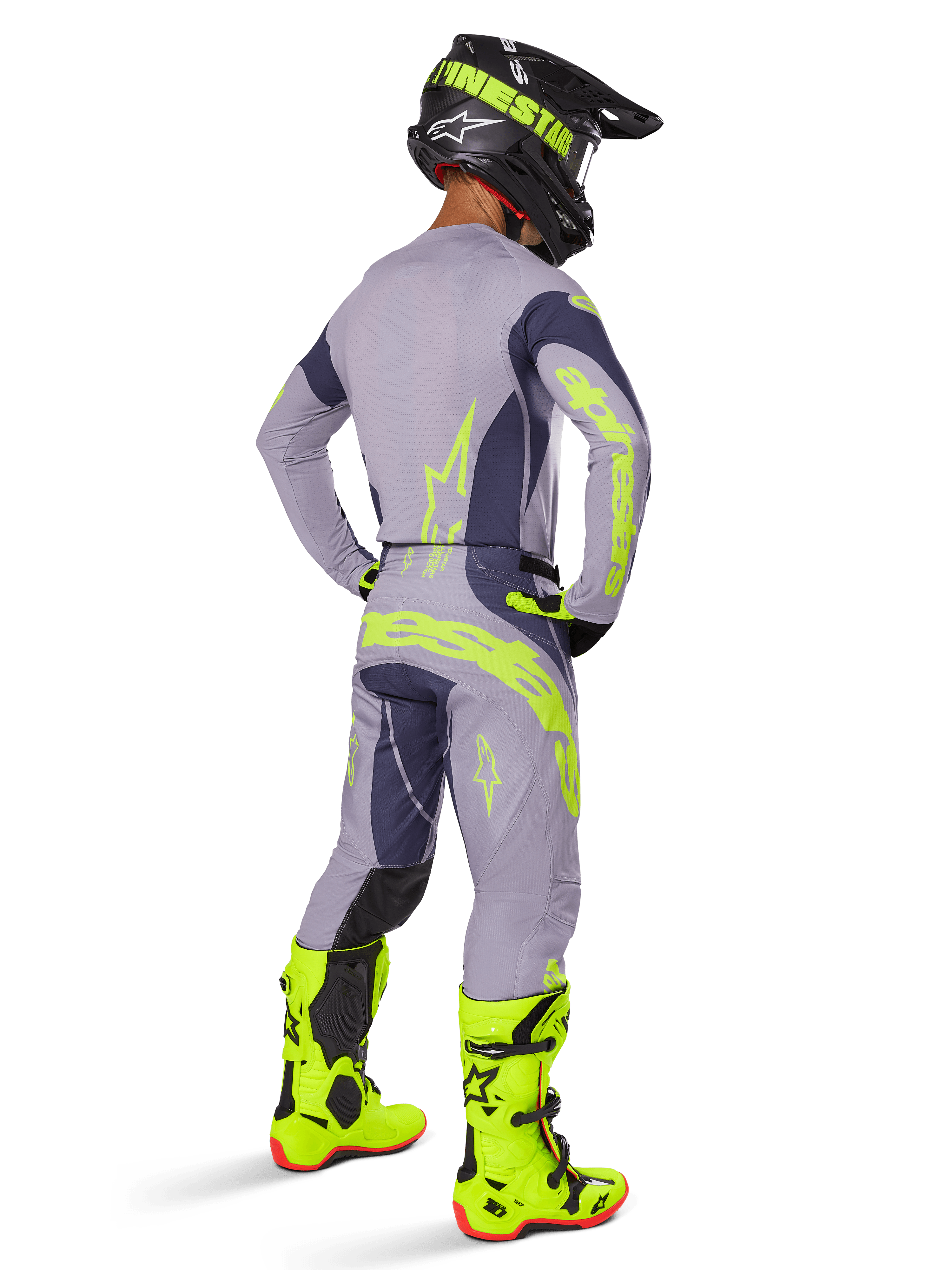 Pilote de motocross vu de dos portant l'ensemble d'équipement Alpinestars Techstar Dreem 2025, gris et gris foncé avec logos jaune fluorescent, maillot et pantalon assortis, casque noir avec accents jaunes et bottes jaune fluorescent vif, tenue de course coordonnée.
