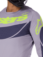 Maillot Alpinestars Techstar Dreem 2025, maillot de motocross, gris et bleu marine avec logo vert citron éclatant, gros plan d'un pilote portant un casque noir, doté de perforations découpées au laser pour la ventilation
