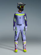 Motocross rider wearing complete Alpinestars 2026 Supertech Scenz racing gear, Purple and Yellow Fluo jersey with matching pants, black helmet with yellow goggles, light purple and neon boots, professional athletic-fit outfit for off-road racing