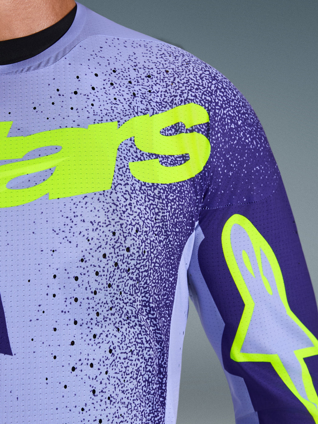 Maillot Alpinestars 2026 Supertech Scenz en violet et jaune fluo, gros plan sur la poitrine et l'épaule montrant les perforations découpées au laser, le matériau en maille extensible et le marquage jaune fluo éclatant pour une performance motocross de niveau professionnel.