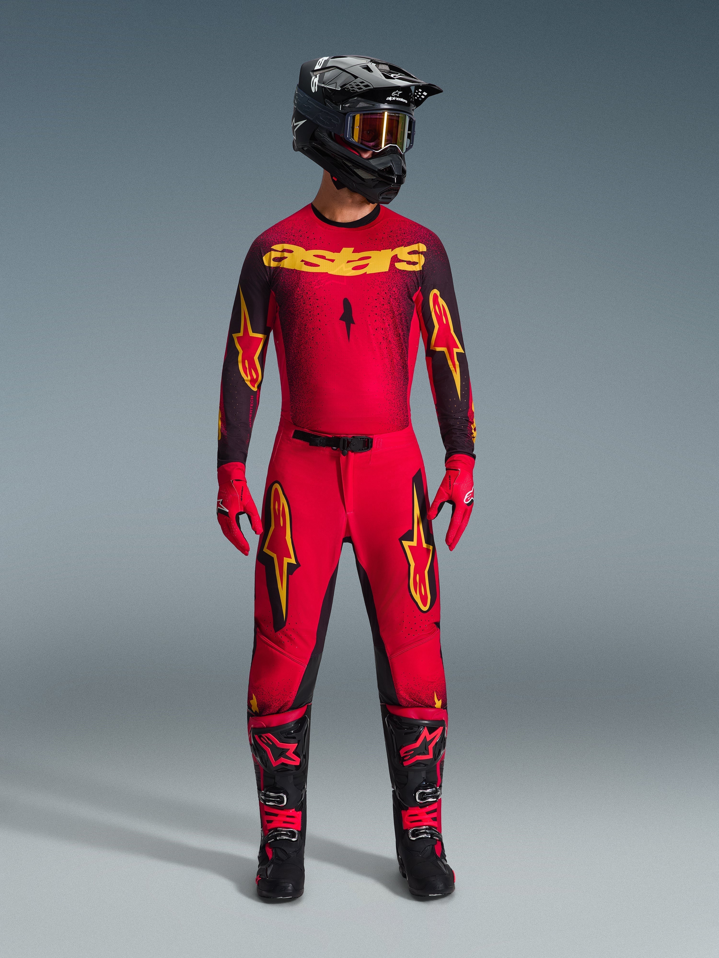 Motocross rider wearing the Alpinestars 2026 Supertech Scenz Jersey in Red Black Yellow, styled with matching pants, black helmet with goggles, red gloves, and black and red boots, professional racing gear set for off-road performance