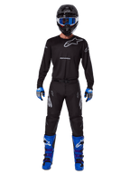 Ensemble d'équipement Alpinestars Racer Graphite 2025, pilote de motocross portant une tenue de course complète, maillot noir à manches longues avec logos Alpinestars gris, pantalon noir, casque noir avec lunettes bleues, gants bleus et gris, bottes bleues et noires, tenue coordonnée pour la compétition de motocross tout-terrain