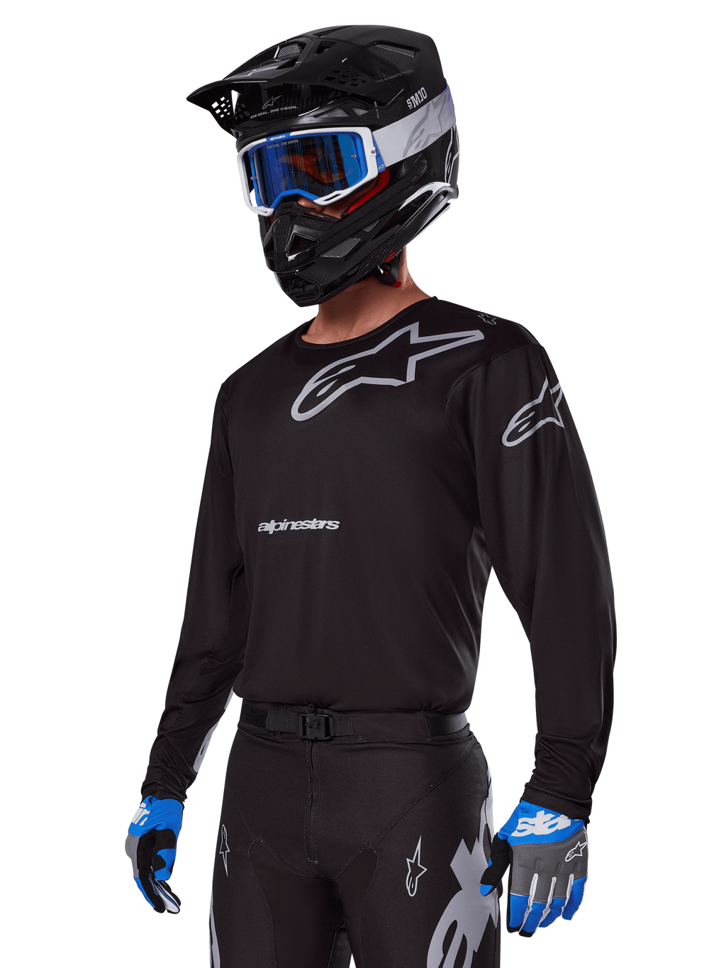 Pilote de motocross portant l'ensemble d'équipement Alpinestars Racer Graphite 2025, maillot noir avec logos Alpinestars gris, pantalon noir assorti avec accents gris, casque noir avec lunettes bleues et blanches, gants bleus et gris, tenue technique épurée pour la course tout-terrain