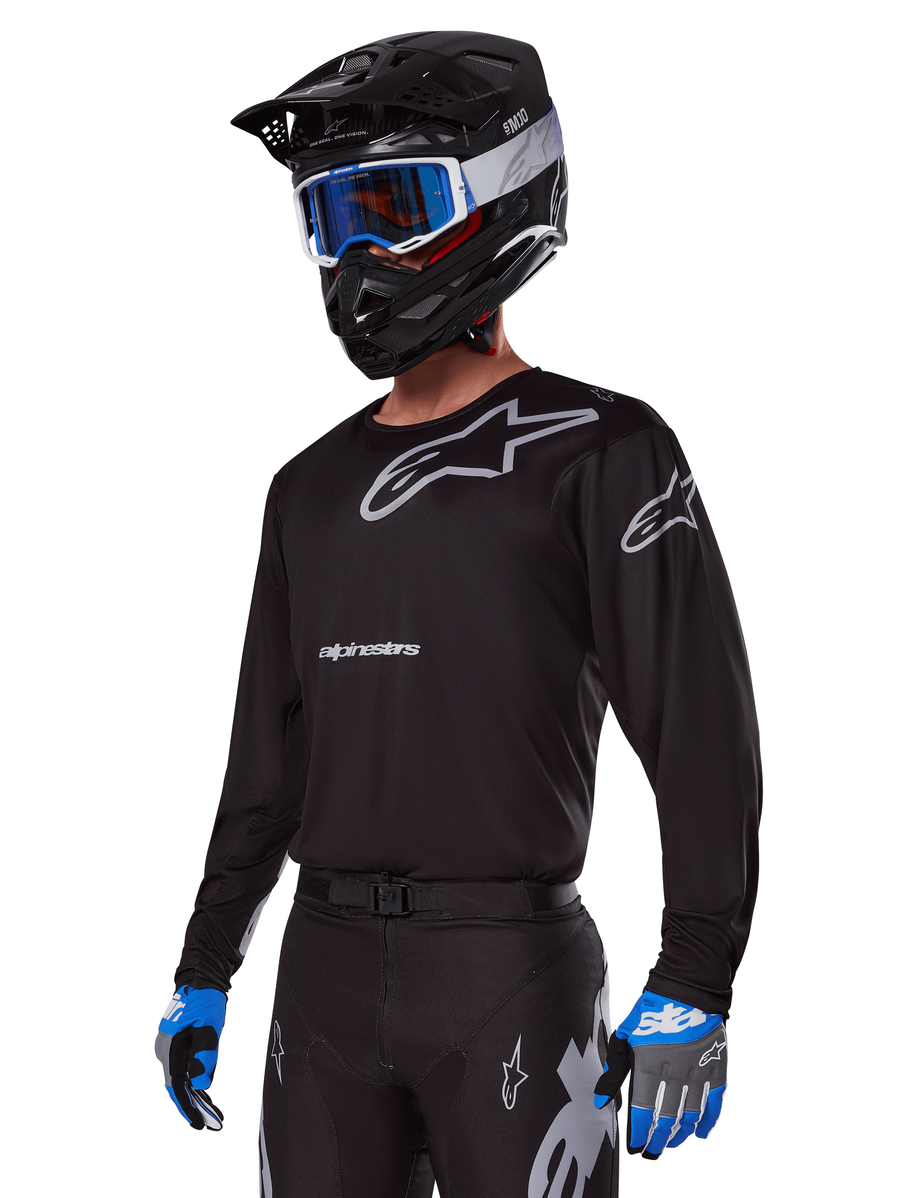 Pilote de motocross portant l'ensemble d'équipement Alpinestars Racer Graphite 2025, maillot noir avec logos Alpinestars gris, pantalon noir assorti avec accents gris, casque noir avec lunettes bleues et blanches, gants bleus et gris, tenue technique épurée pour la course tout-terrain