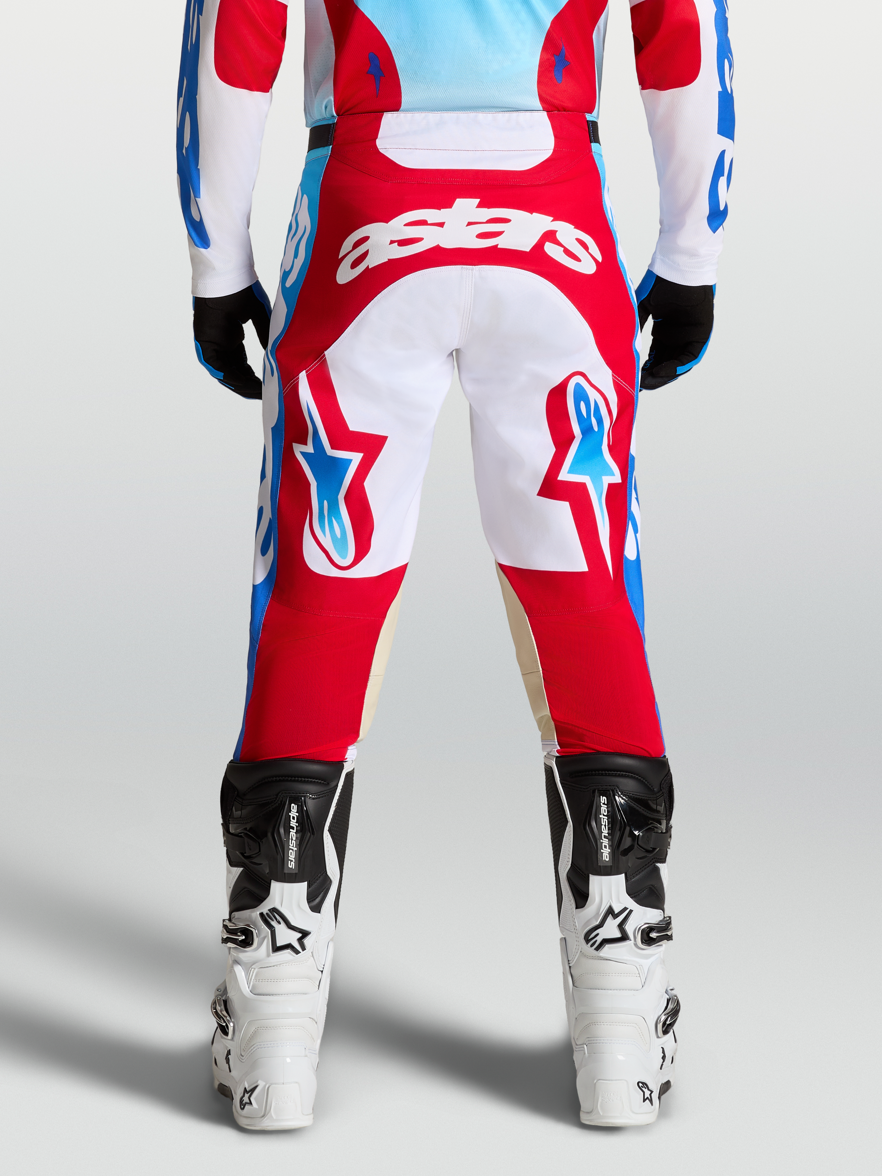 Alpinestars Racer Hunt Pants, red and white motocross pants shown from the rear on a rider, featuring light blue accents and ergonomic pre-curved leg construction.
