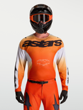 Maillot Racer Amber Alpinestars, maillot de motocross pour homme, orange et blanc, porté avec un casque de moto noir, tissu technique léger évacuant l'humidité, idéal pour le tout-terrain et la course.