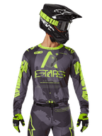 Maillot Alpinestars 2025 Racer Hollow, maillot de motocross, camouflage sombre et jaune fluo, porté avec pantalon assorti, casque noir et jaune avec masque et gants noirs, avec logo Alpinestars et motif camouflage