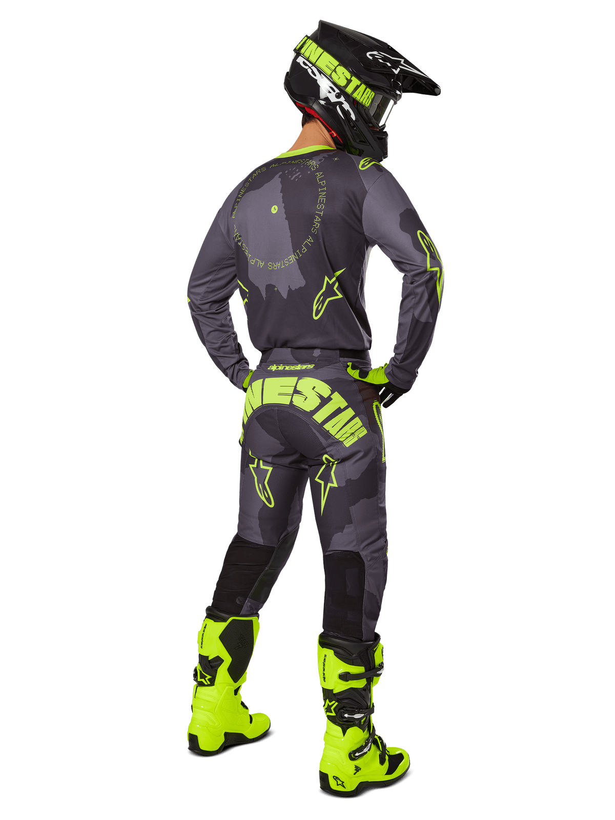 Vue arrière d'un pilote de motocross portant l'ensemble Racer Hollow 2025 en Dark Camo Yellow Fluo, comprenant un maillot camouflage gris avec des accents jaune fluo, un pantalon de motocross assorti avec un marquage imposant sur l'assise, des bottes jaune fluo vif et un casque noir avec des lunettes jaunes.