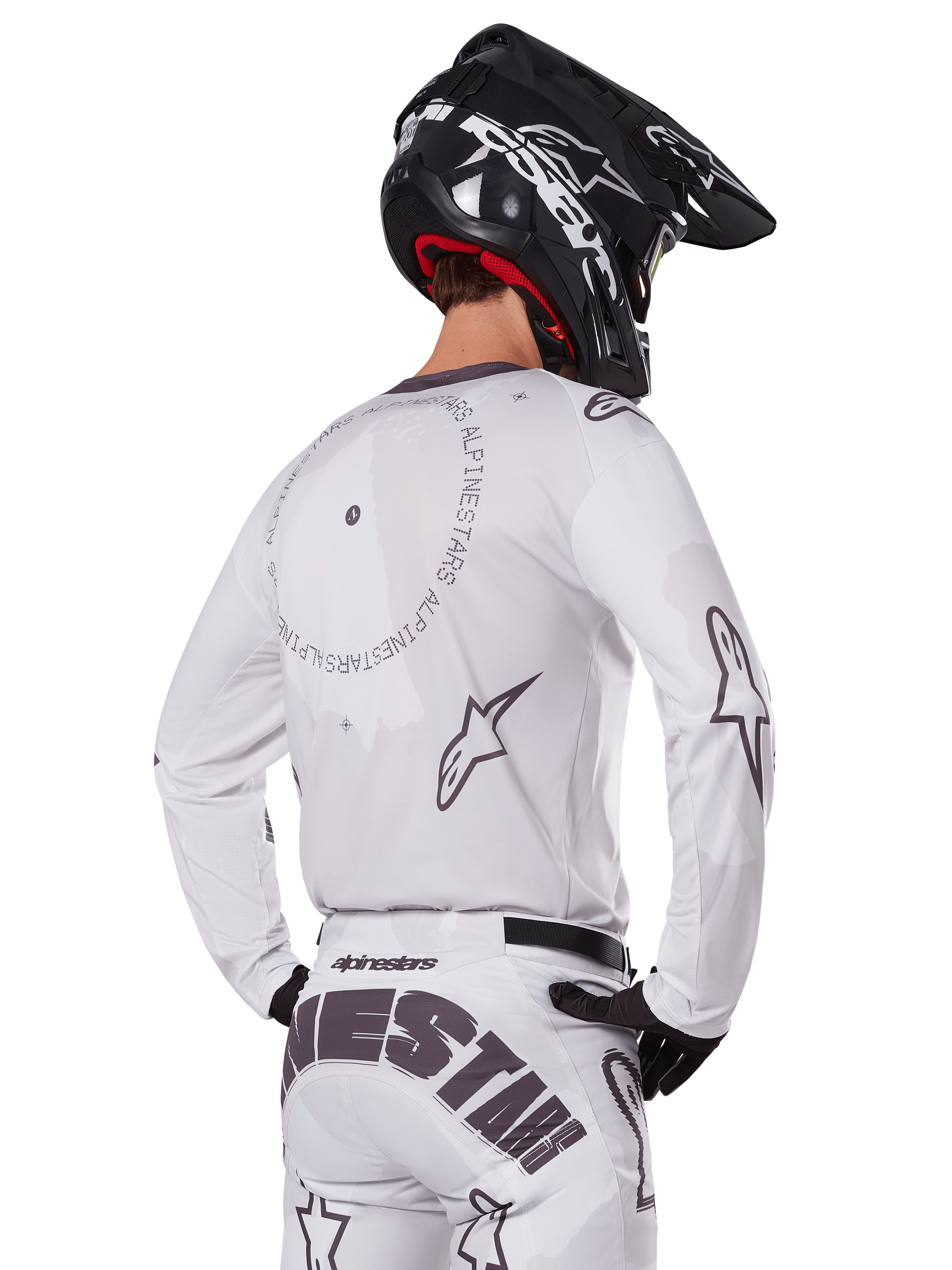 Motocross rider from the back wearing the Alpinestars 2025 Racer Hollow Gear Set in White, white long-sleeve jersey with grey star logos and circular graphics, matching white pants with bold branding on the seat, black helmet, coordinated off-road racing gear.