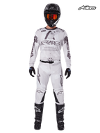 Tenue Complète Racer Hollow 2025 d'Alpinestars, maillot et pantalon de motocross pour homme en blanc et marron clair, vue studio de face sur un modèle portant un casque, des gants et des bottes assortis