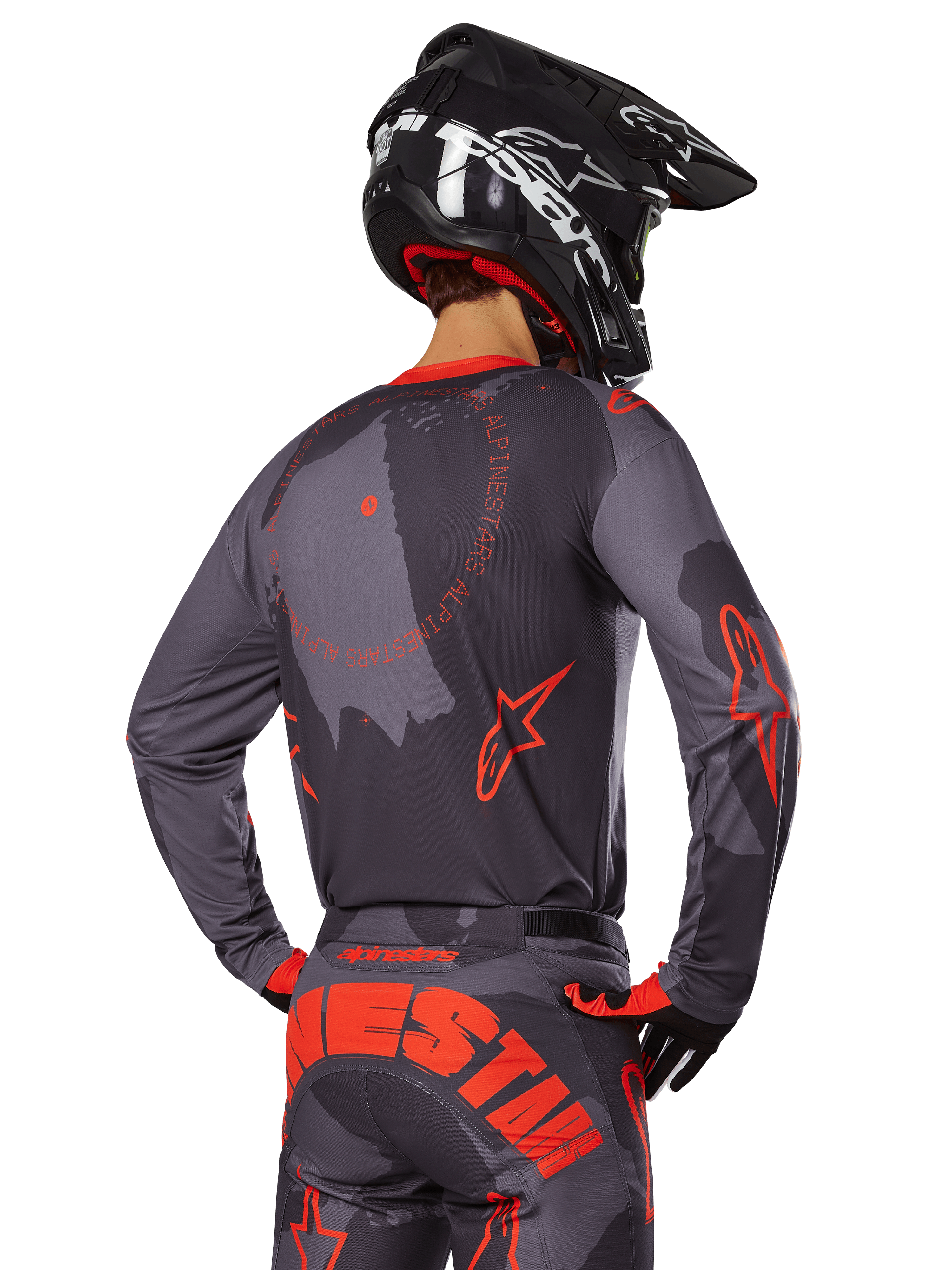 Maillot Alpinestars Racer Hollow 2025, vue arrière d'un pilote de motocross en tenue Gris Camo et Orange Fluo, avec un pantalon camouflage assorti arborant un grand lettrage Alpinestars orange et un casque noir, design d'équipement tout-terrain professionnel