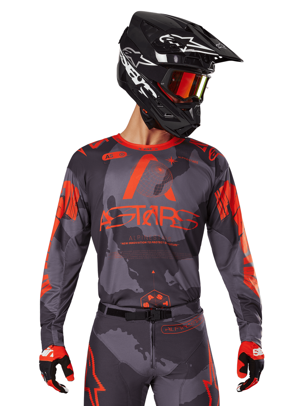 Alpinestars 2025 Racer Hollow Jersey, maillot de motocross, camouflage gris et orange fluo, porté avec une tenue assortie incluant un pantalon et des gants, doté d'un casque noir avec des graphismes blancs et des lunettes de protection, logo ASTARS audacieux, vêtement de sport de protection pour la course tout-terrain