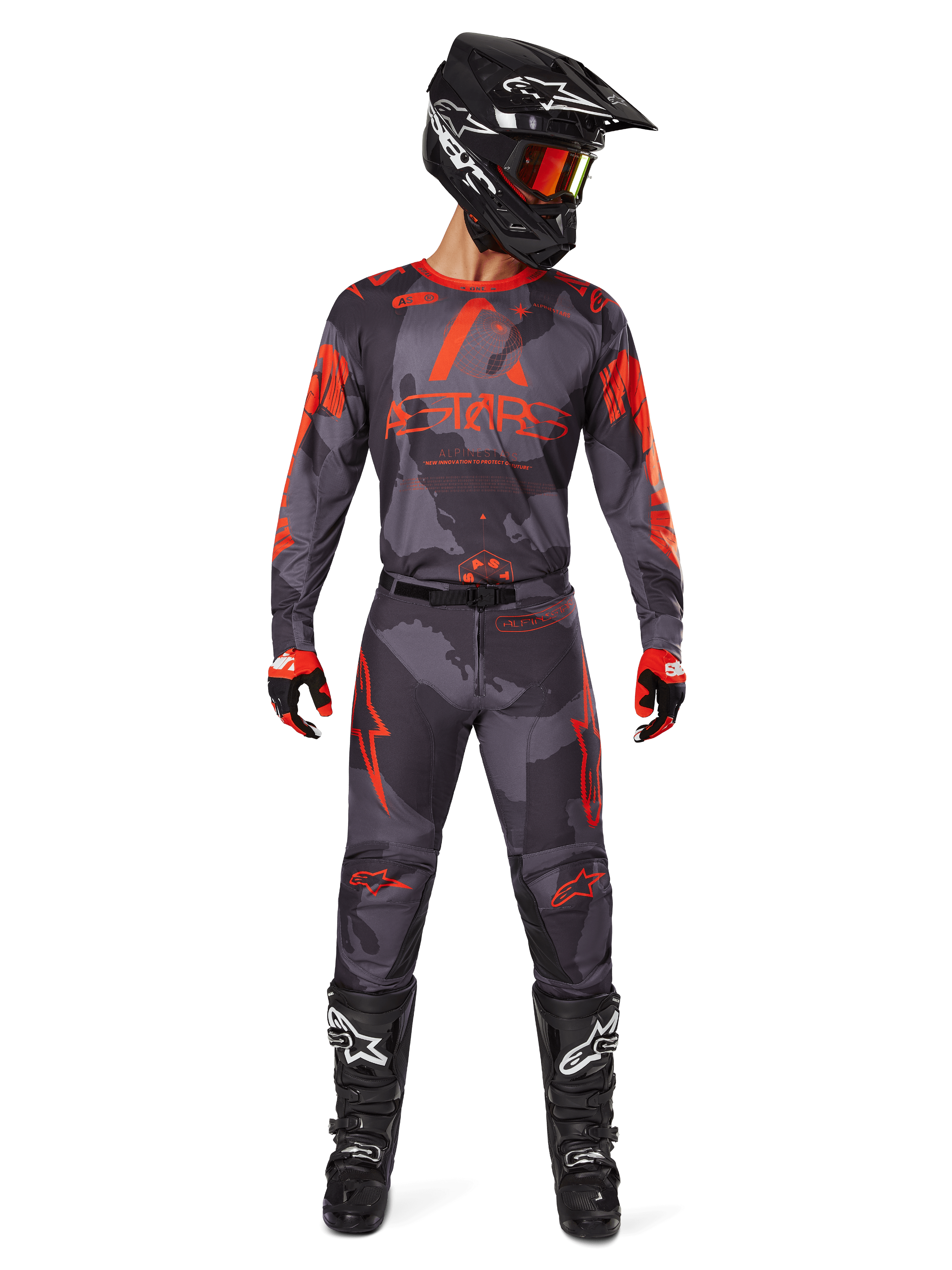 Pilote de motocross portant le maillot Alpinestars Racer Hollow 2025 et le pantalon assorti en Gris Camo Orange Fluo, tenue complète avec casque, lunettes, gants et bottes noirs, avec logos orange vifs et motif camouflage.