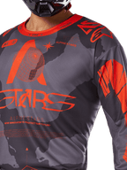 Maillot Alpinestars Racer Hollow 2025, maillot de motocross, camouflage gris et orange fluo, avec un large logo Alpinestars orange et des graphismes techniques, col rond, conçu pour la performance en conduite tout-terrain