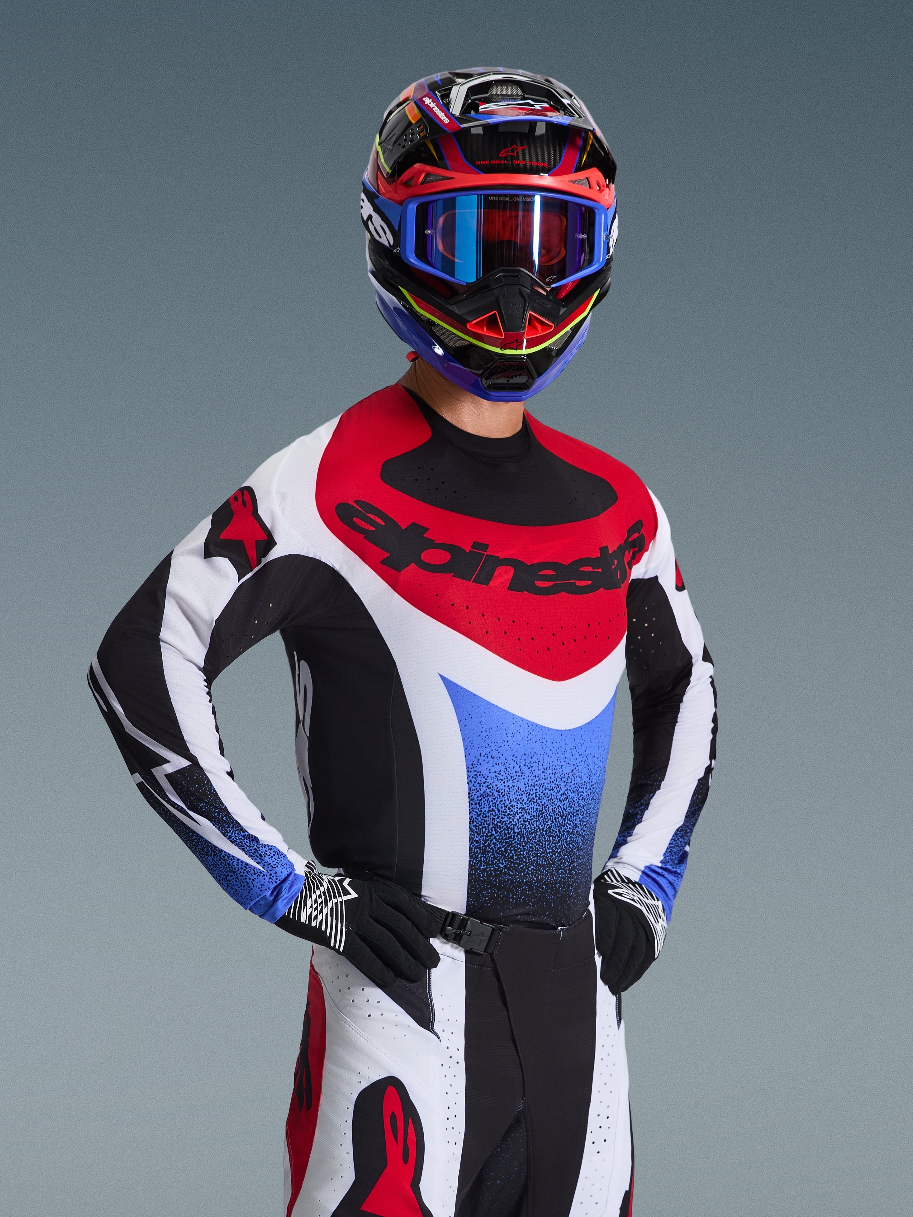 Alpinestars 2026 Techstar Knif Gear Set, pilote de motocross en maillot de course rouge, blanc et bleu avec accents noirs, casque et lunettes multicolores assortis, gants noirs, équipement professionnel pour la compétition de motocross.