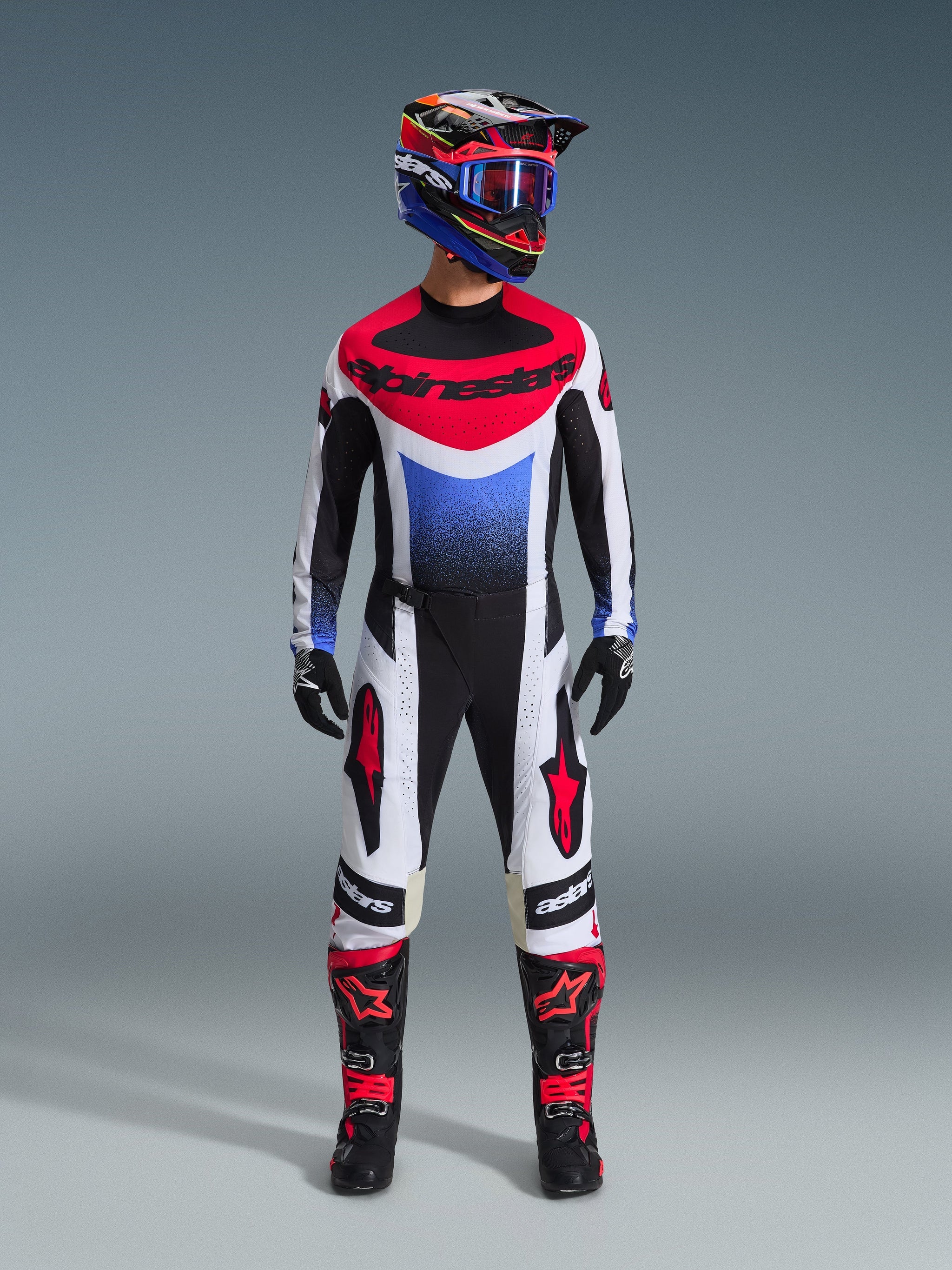 Alpinestars 2026 Techstar Knif Jersey, Motocross Jersey in White, Black, Red, and Blue with a blue gradient graphic, worn as part of a complete off-road racing kit including matching pants, black and red boots, and a coordinating helmet with goggles.