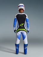 Alpinestars 2026 Techstar Knif Gear Set, back view of a motocross rider in Ucla Blue, Black, and White, featuring Yellow Fluo branding on the jersey and pants, paired with blue racing boots and a white helmet.