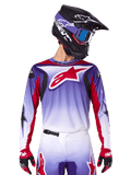 Maillot Alpinestars Fluid Wurx 2025, maillot de motocross, dégradé du violet au blanc, logo étoile rouge et accents rouges, coupe athlétique, porté avec le pantalon assorti, un casque noir et des gants rouges
