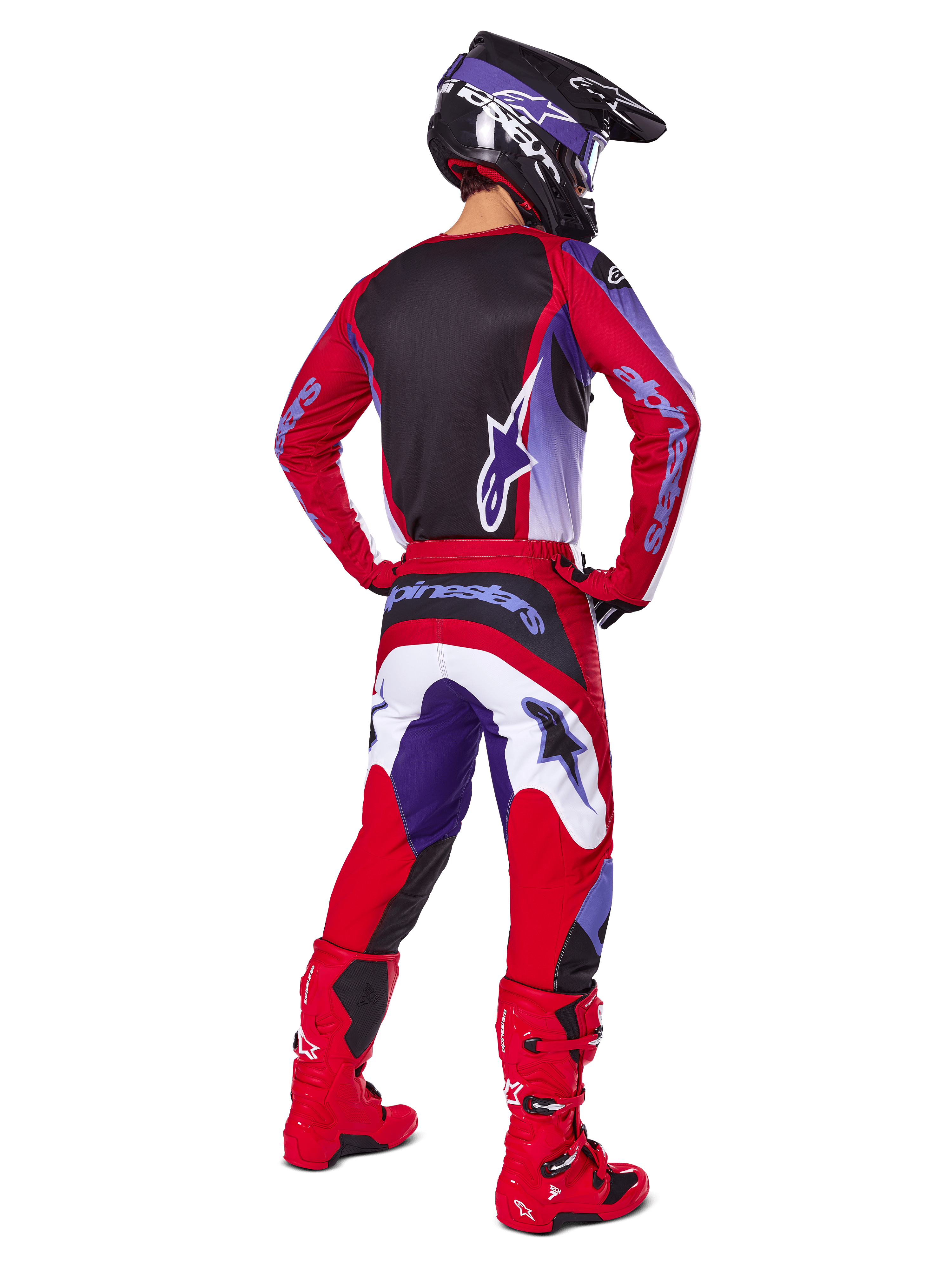 Pilote de motocross de dos portant l'ensemble Alpinestars 2025 Fluid Wurx, maillot Purple Bright Red avec panneau arrière noir, pantalon de motocross assorti avec accents blancs et violets, bottes rouge vif et casque noir, tenue de course tout-terrain professionnelle