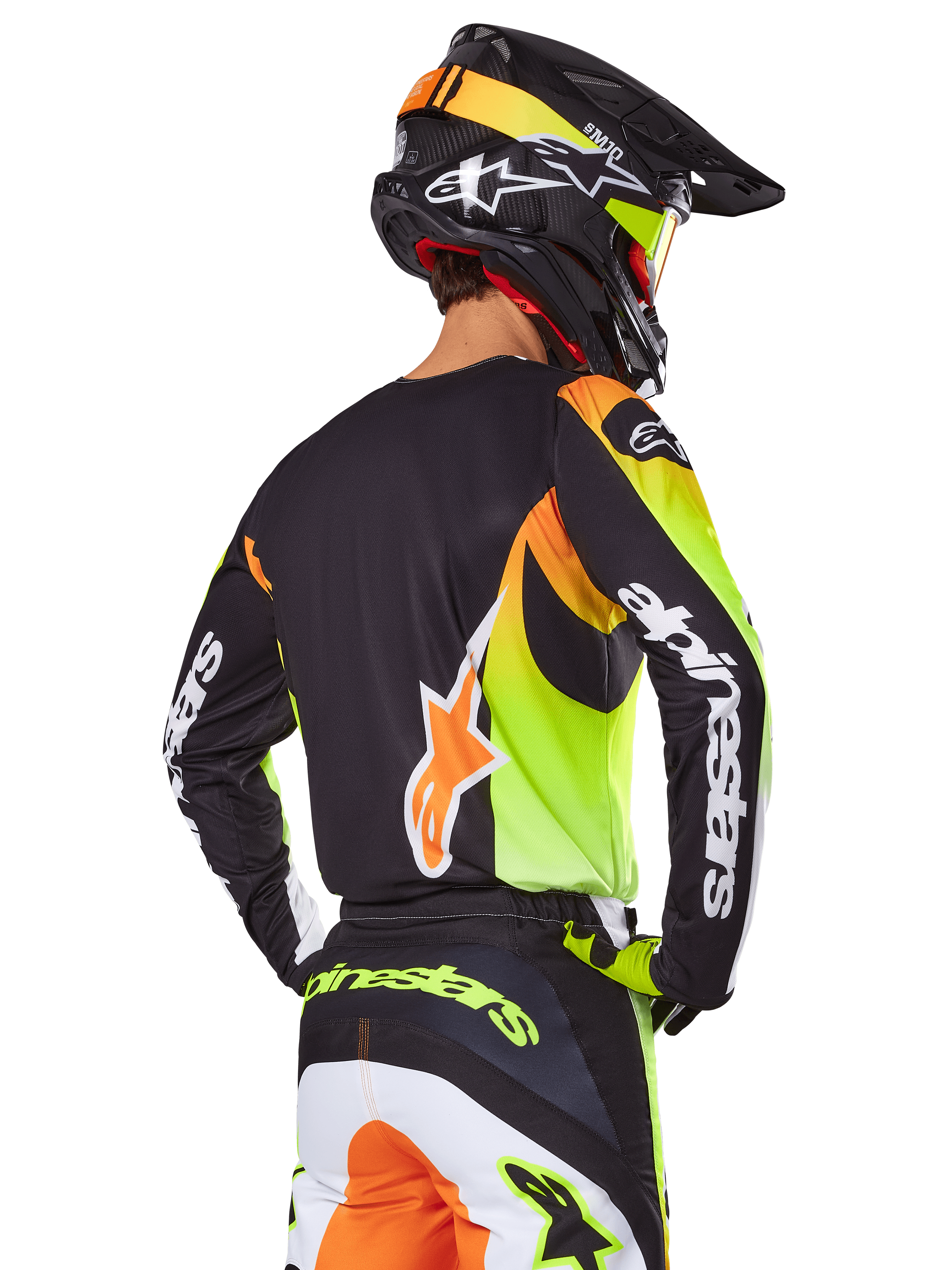 Motocross rider from behind wearing the Alpinestars 2025 Fluid Wurx Gear Set, black jersey with vibrant neon yellow and orange graphics, matching pants with white and orange panels, black helmet with neon accents, bold Alpinestars branding on sleeves and seat