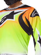 Maillot Alpinestars Fluid Wurx 2025, maillot de motocross, jaune fluorescent avec motifs noirs et orange, arborant un grand logo Alpinestars noir sur la poitrine et l'épaule, porté par un pilote avec un casque noir.