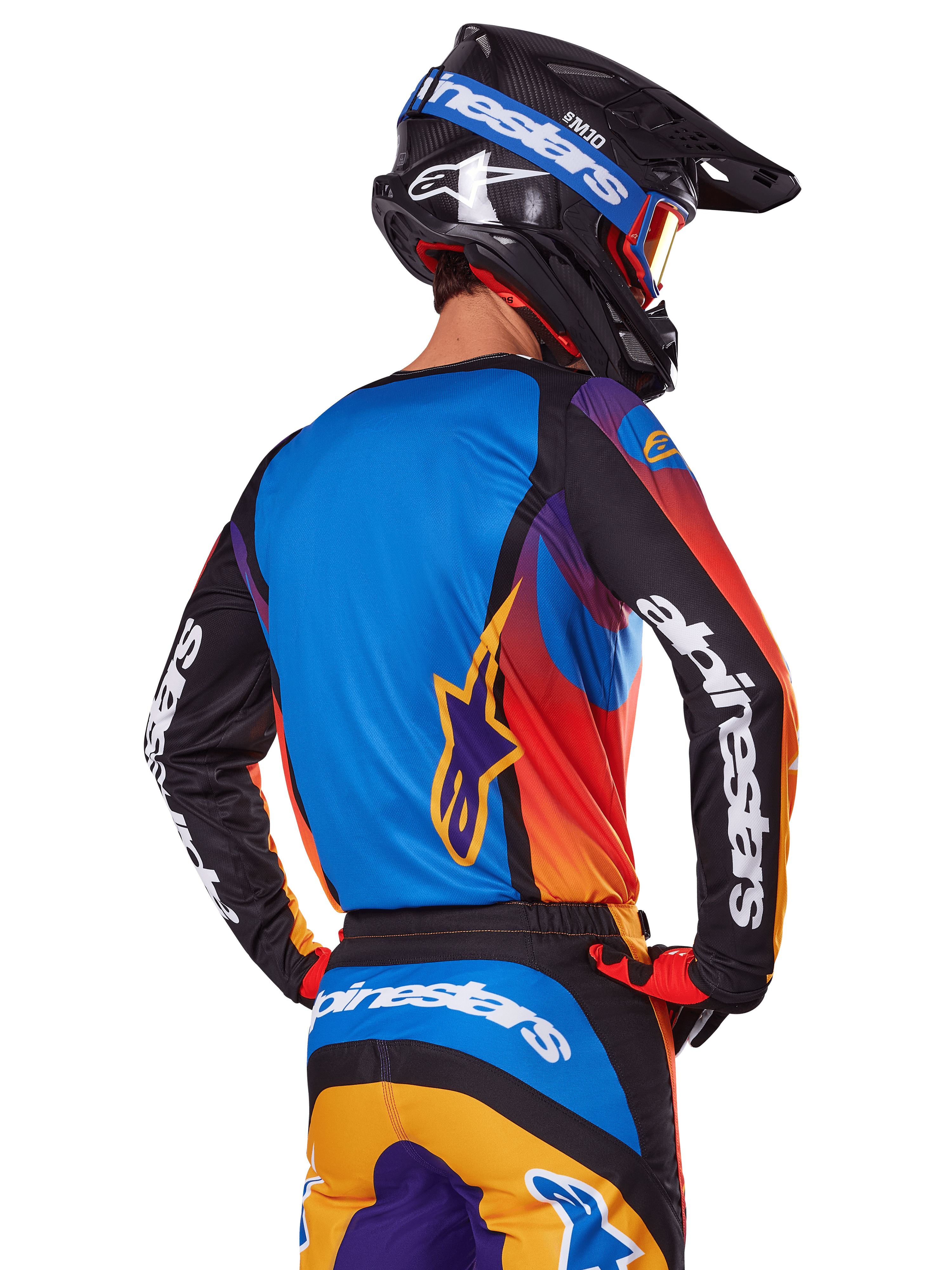 Motocross rider viewed from the back wearing the Alpinestars 2025 Fluid Wurx Gear Set, multicolor jersey with blue back and black sleeves featuring white logos, matching orange and blue pants, black and blue helmet with orange goggles, coordinated off-road racing outfit.