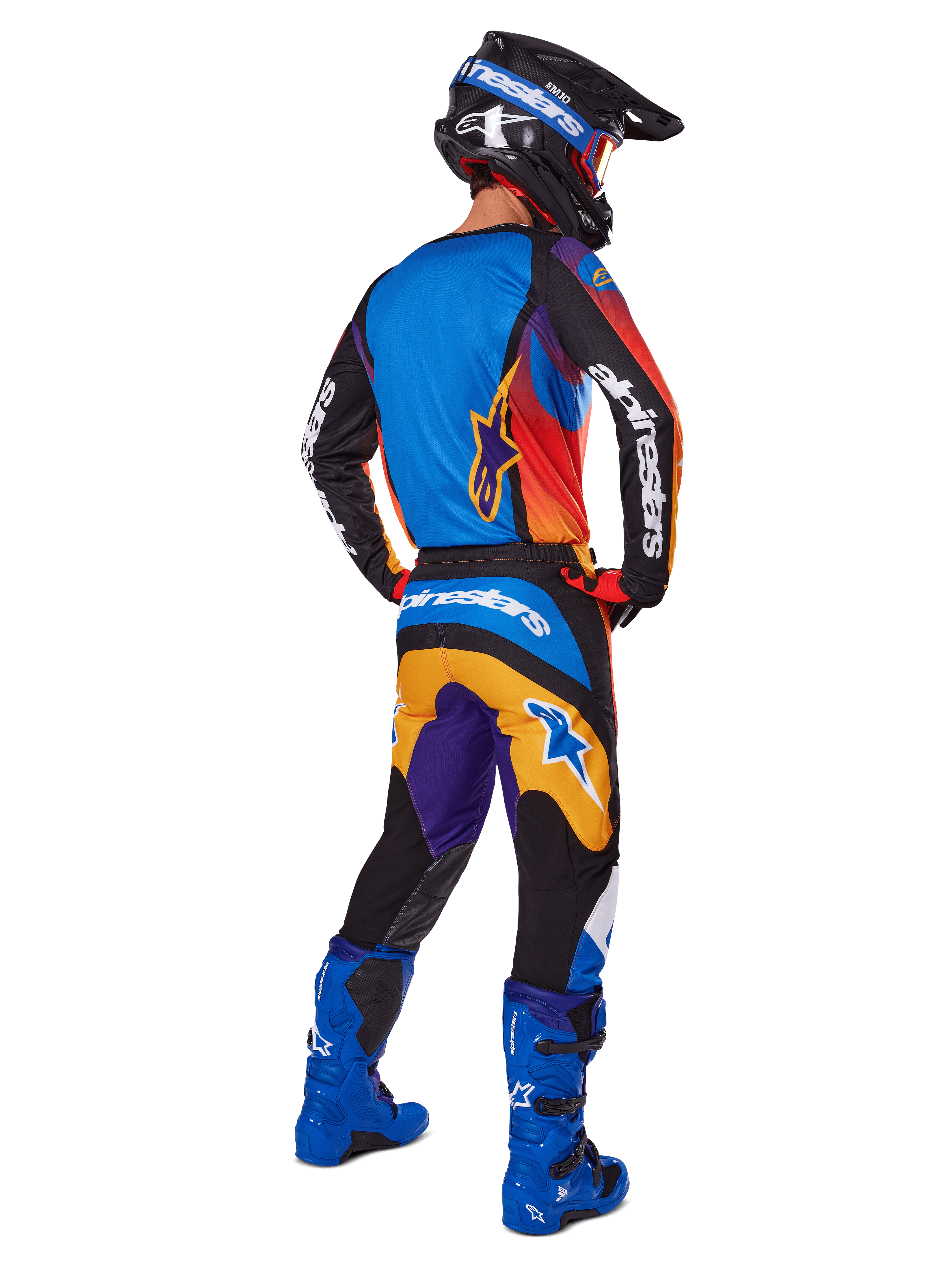 Motocross rider viewed from the back wearing Alpinestars 2025 Fluid Wurx Gear Set, multicolor jersey with blue orange and purple panels, matching pants with white Alpinestars logo on the seat, bright blue boots and a black helmet, coordinated outfit for off-road racing