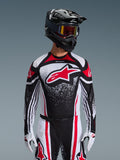 Alpinestars 2026 Techstar Nomur Jersey, Motocross Jersey, Black White and Red, worn by a rider with matching pants, black helmet, and white gloves, featuring a large red Astars logo and speckled graphic design, athletic race fit for off-road competition