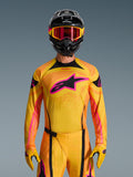 Maillot Techstar Nomur 2026 en Orange Jaune Rose, porté par un pilote de motocross avec un casque noir assorti et des lunettes roses, arborant un grand logo Alpinestars rose sur la poitrine, coupe athlétique de course pour une performance tout-terrain.