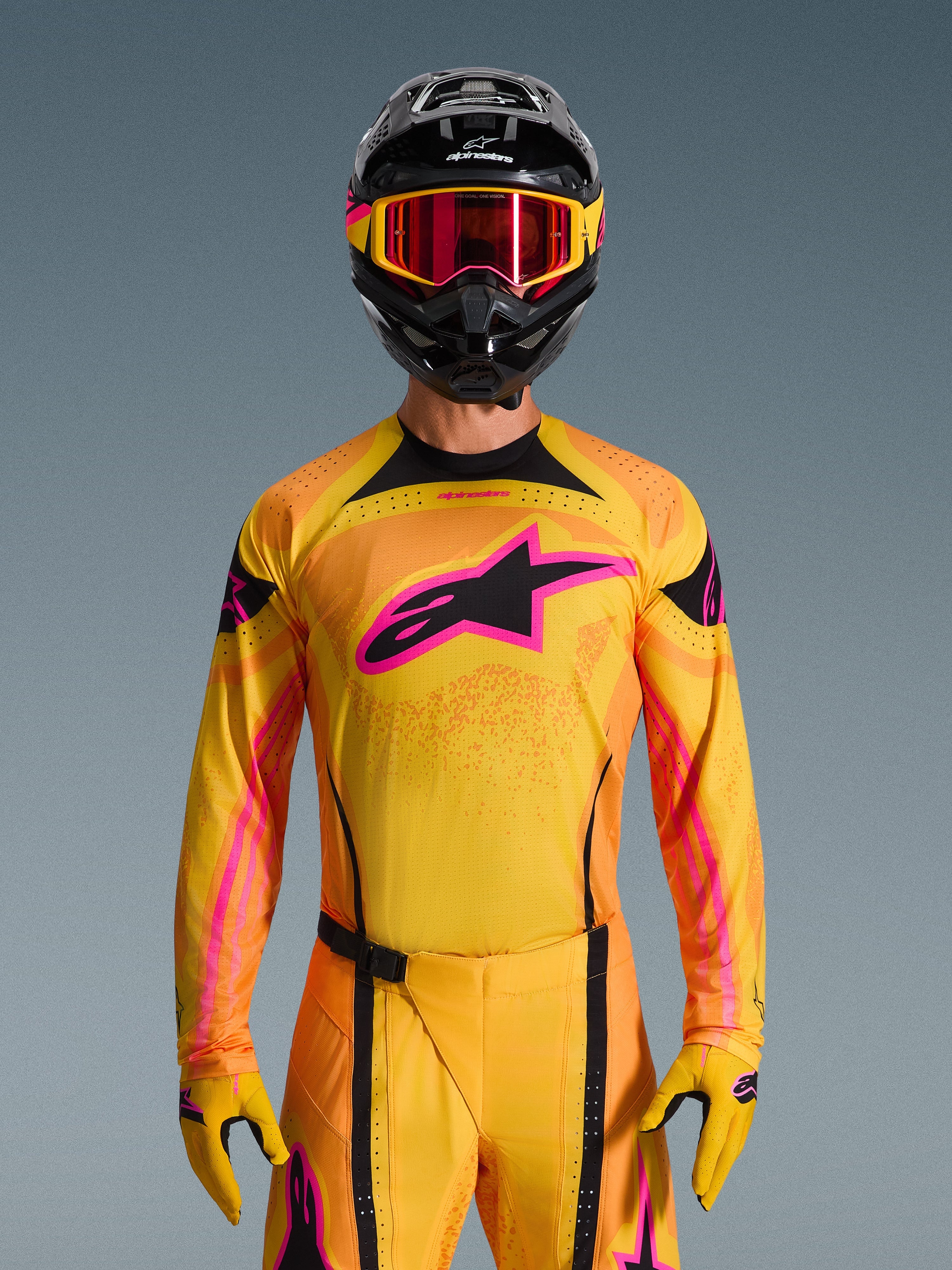 Maillot Techstar Nomur 2026 en Orange Jaune Rose, porté par un pilote de motocross avec un casque noir assorti et des lunettes roses, arborant un grand logo Alpinestars rose sur la poitrine, coupe athlétique de course pour une performance tout-terrain.