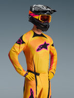 Maillot Alpinestars Techstar Nomur 2026, maillot de motocross, orange, jaune et rose, porté par un pilote avec un casque et des lunettes noirs assortis, doté d'un grand logo d'étoile rose sur la poitrine, d'accents noirs et de détails de ventilation découpés au laser.