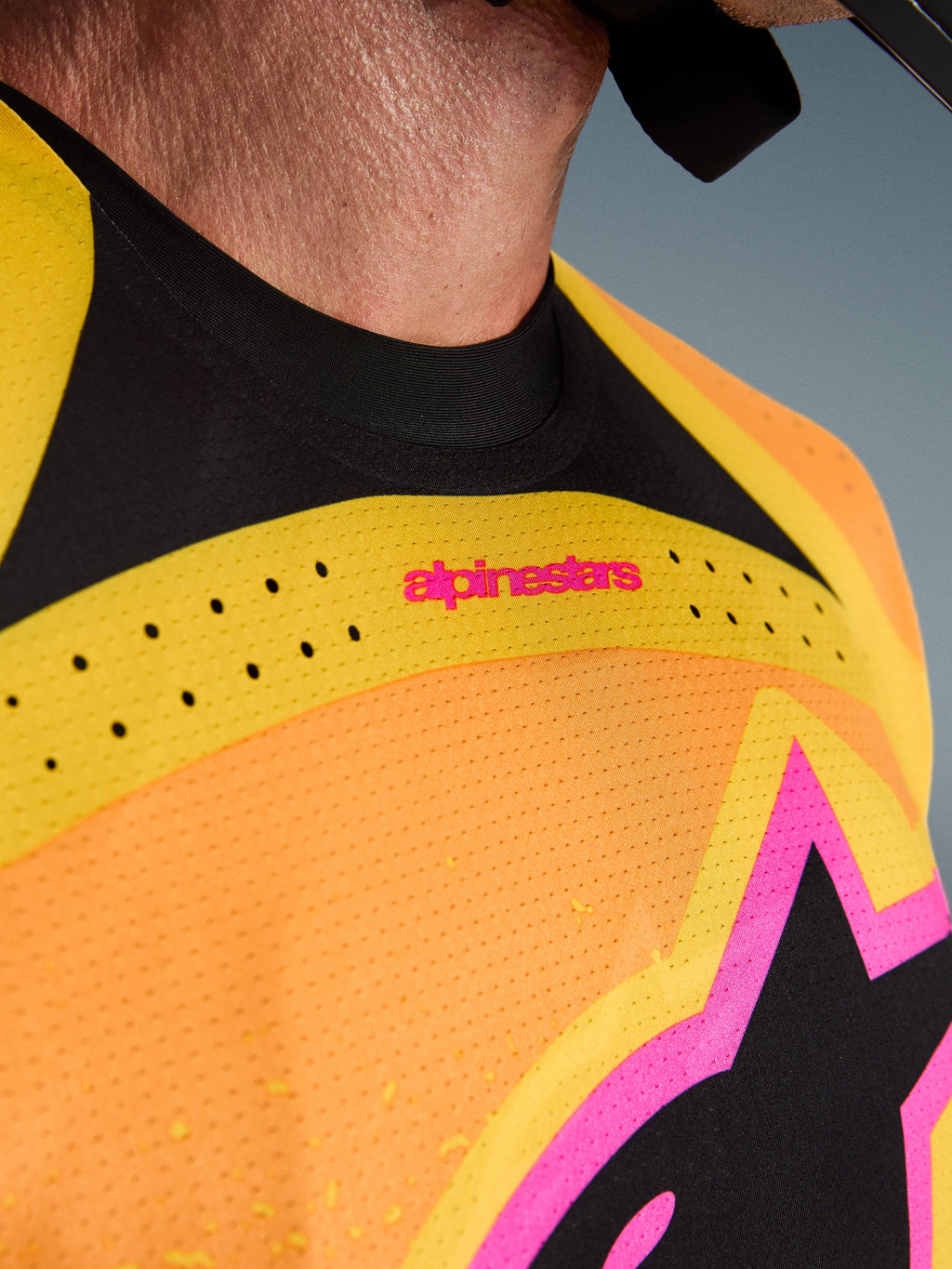 Alpinestars 2026 Techstar Nomur Jersey, maillot de motocross, orange, jaune et rose, gros plan sur la poitrine et le col, avec perforations laser, logo rose et tissu en maille respirante