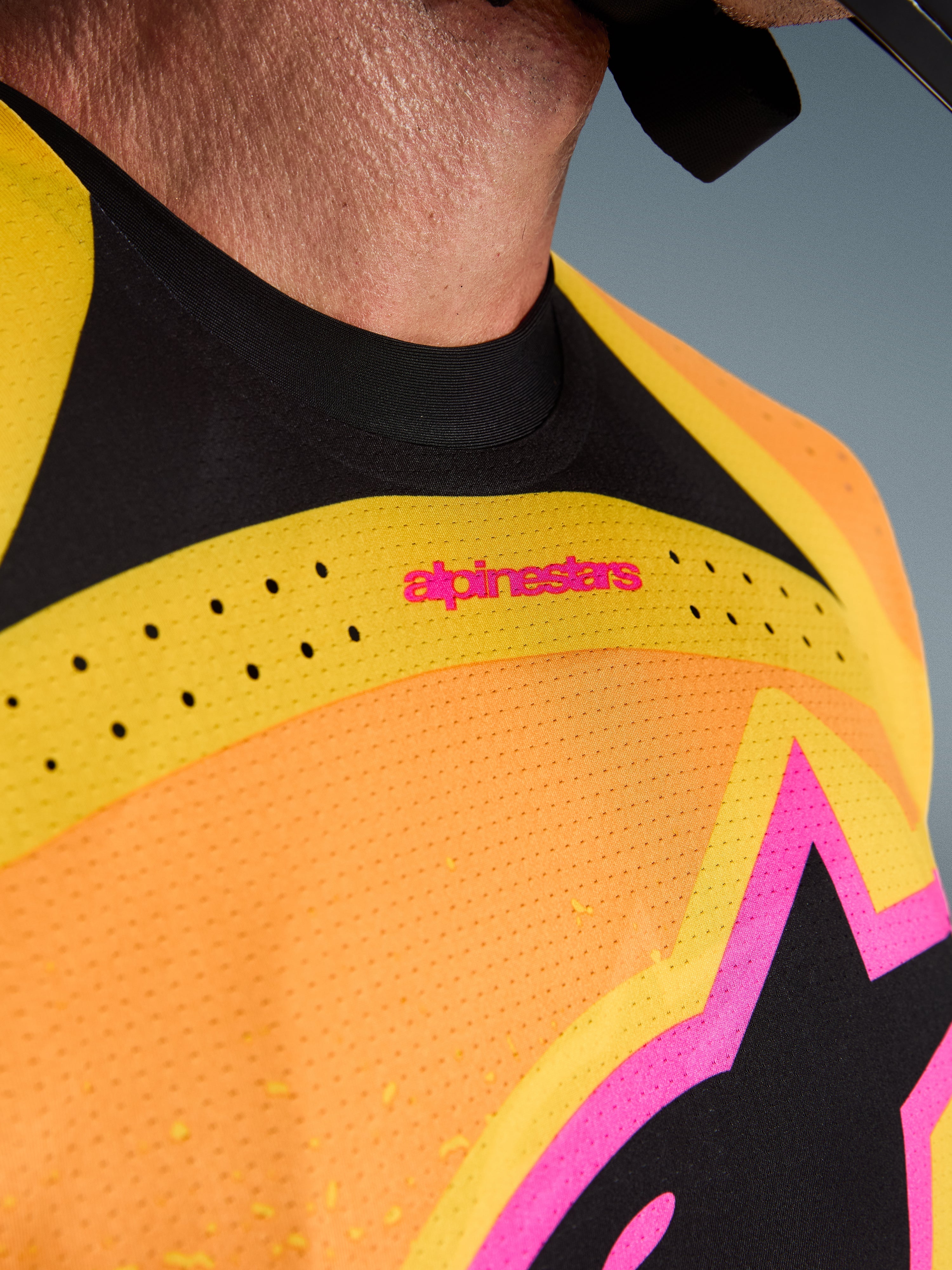 Alpinestars 2026 Techstar Nomur Jersey, maillot de motocross, orange, jaune et rose, gros plan sur la poitrine et le col, avec perforations laser, logo rose et tissu en maille respirante