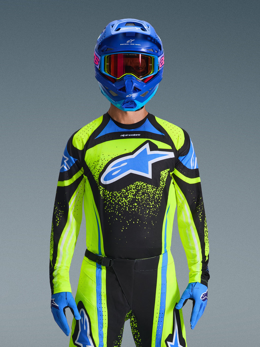 Alpinestars 2026 Techstar Nomur Gear Set, motocross rider wearing black, neon yellow, and blue jersey with matching pants and gloves, blue helmet with reflective goggles, professional racing outfit for off-road competition, front view