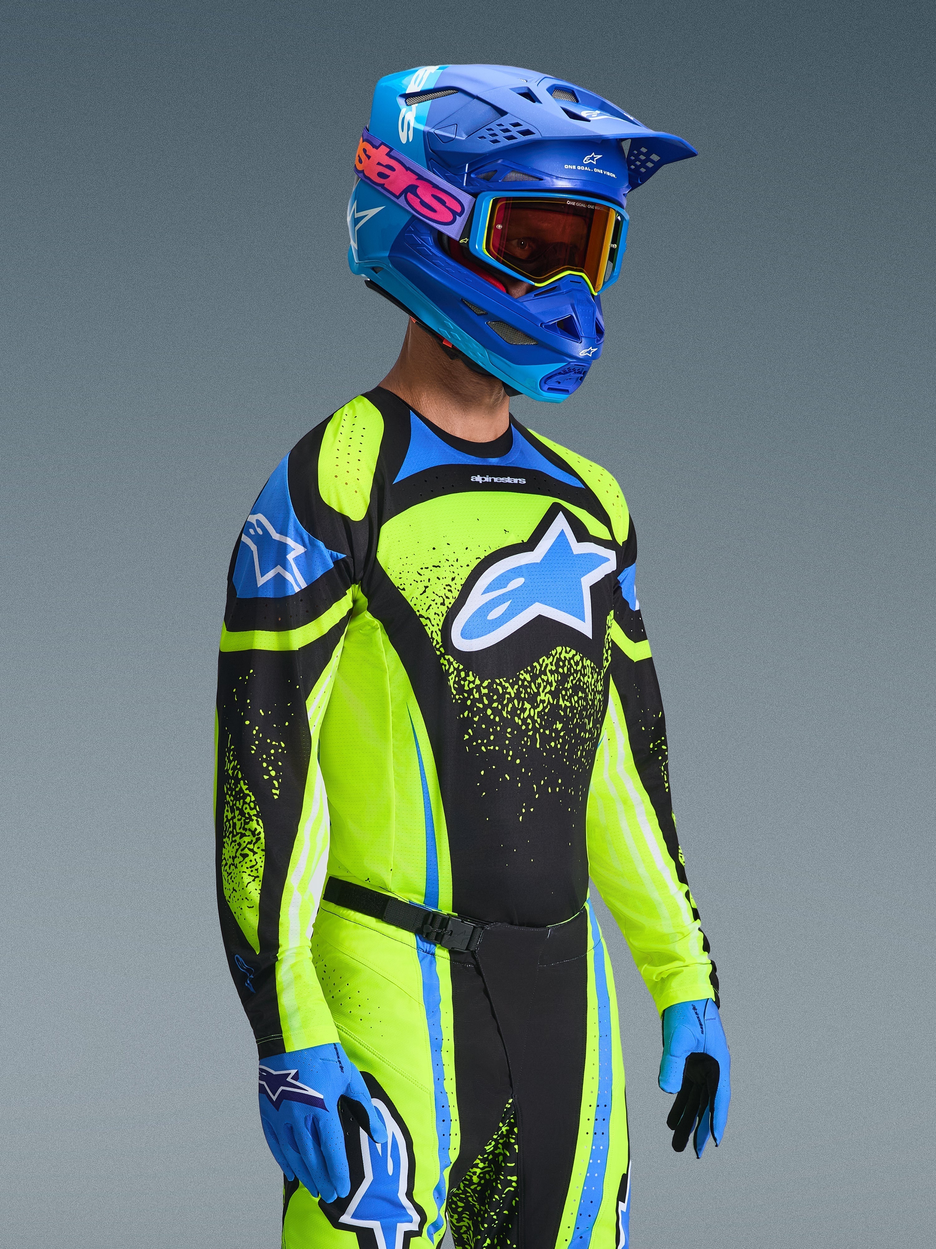 Motocross rider wearing the Alpinestars 2026 Techstar Nomur Gear Set, Neon Yellow and Blue jersey with black panels, large blue and white logo on chest, matching blue helmet with orange goggles, blue and black gloves, coordinated high-performance gear for off-road racing