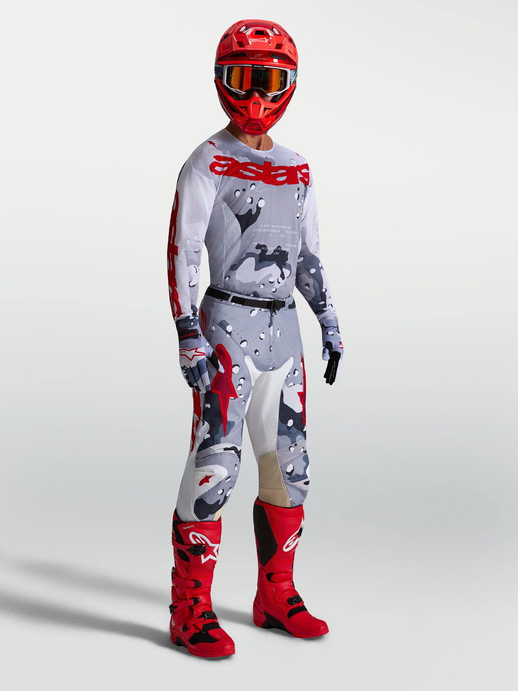 Maillot Racer Air Lone Alpinestars, maillot de motocross pour homme, gris camouflage et rouge feu, mesh respirant, porté par un pilote avec une tenue de protection complète.