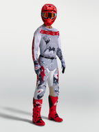 Maillot Racer Air Lone Alpinestars, maillot de motocross pour homme, gris camouflage et rouge feu, mesh respirant, porté par un pilote avec une tenue de protection complète.